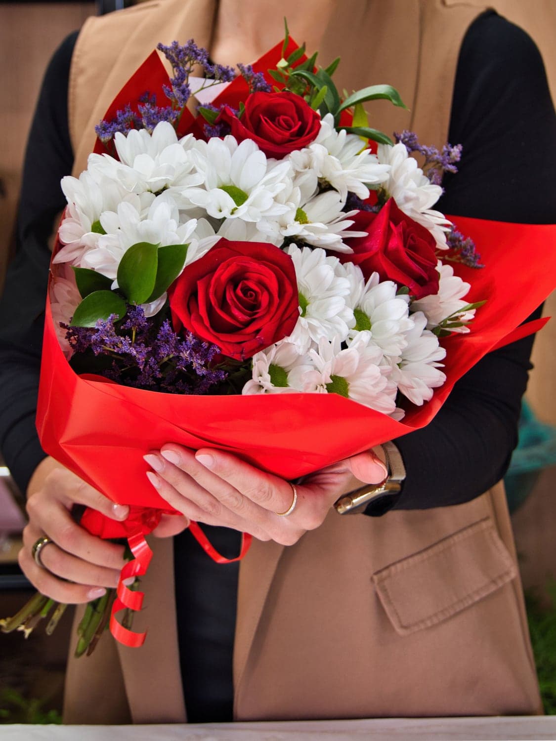 Floristka z Květiny spolu drží kytici z červených růží a bílých chryzantém v červeném papíru